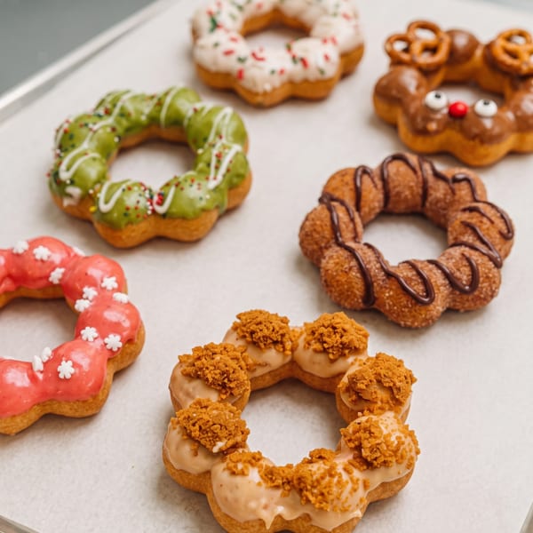 Variety of colorful mochi donuts with different glazes and toppings, including a reindeer donut, on a tray.
