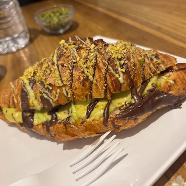 Croissant filled with pistachio cream, drizzled with chocolate, and topped with crushed pistachios.