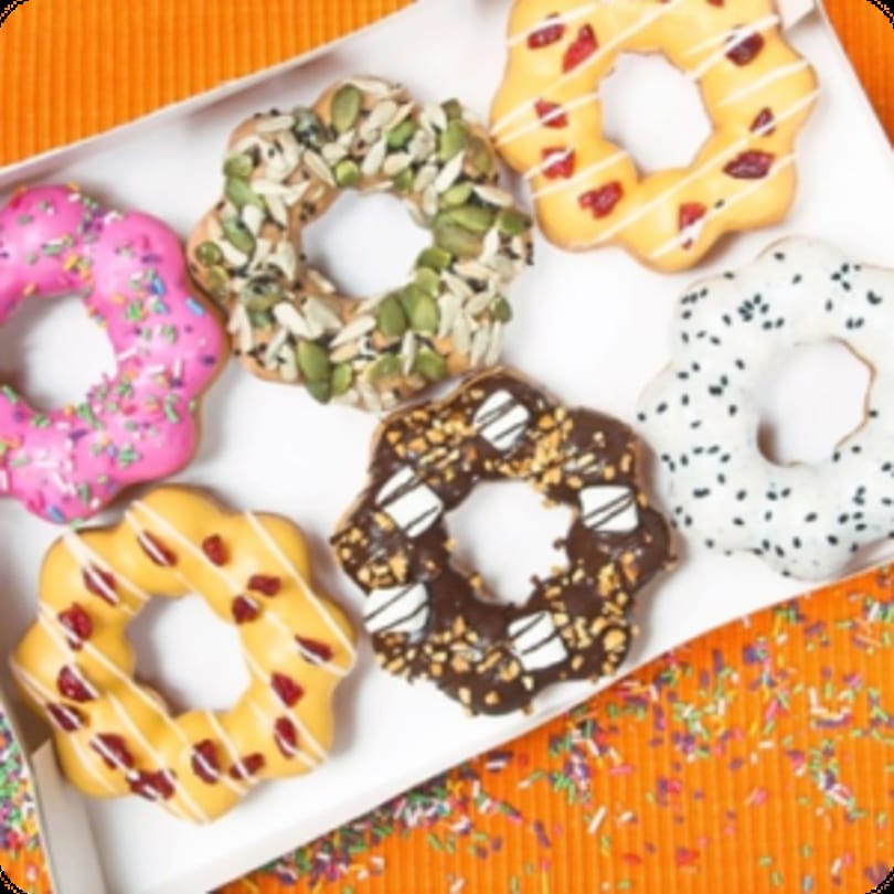 A box of six colorful, star-shaped donuts with various toppings on an orange background.