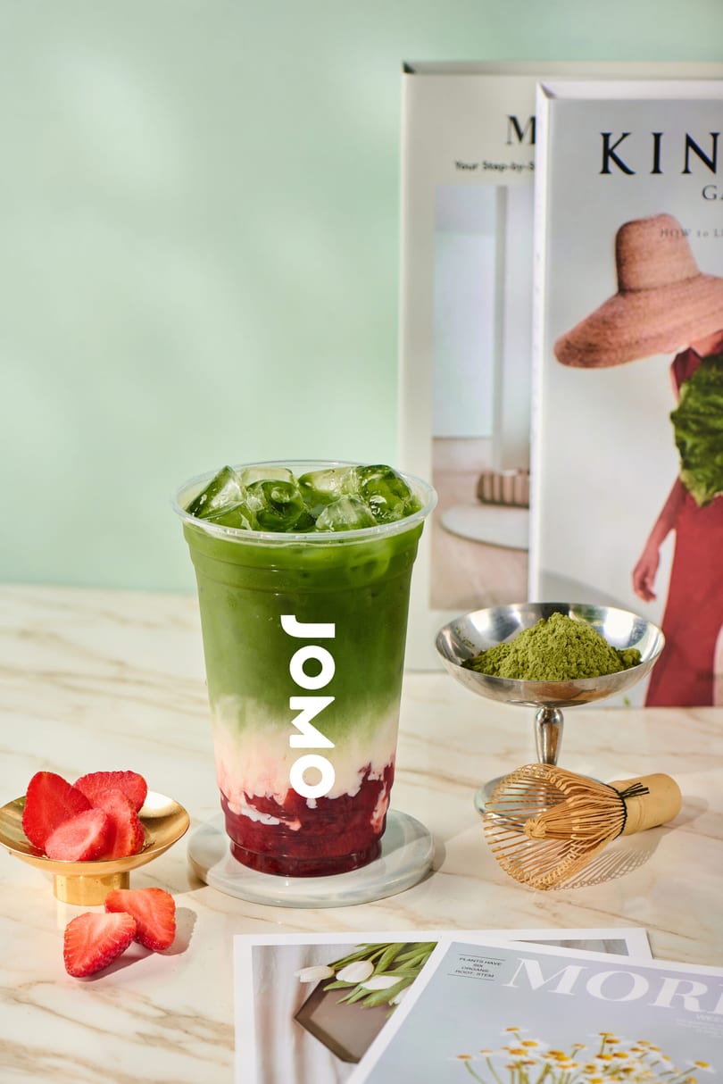 A JOMO matcha strawberry drink with ice, fresh strawberries, and matcha powder on a marble table.